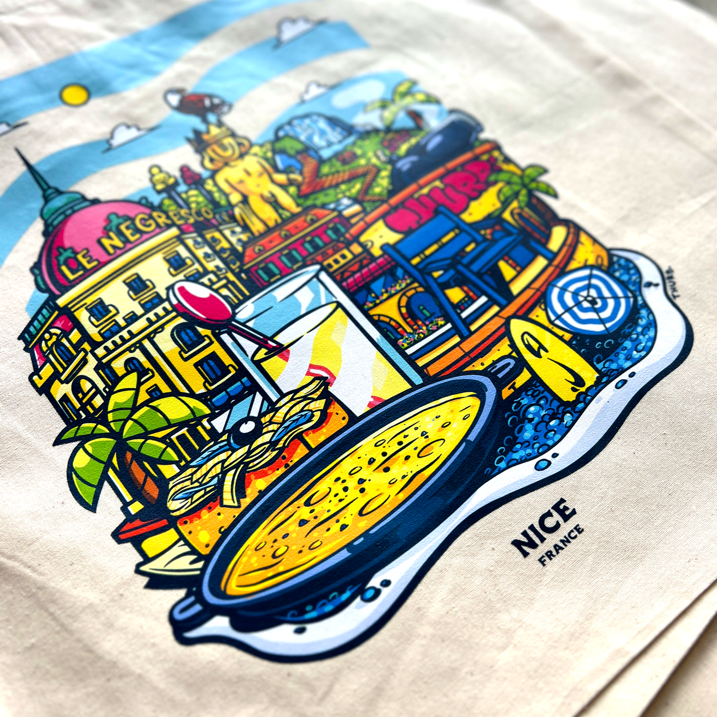 Tote bag avec une image de la ville de Nice avec pleins d'éléments représentants la ville comme des boissons, des plats et des monuments.